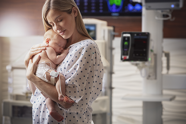 parent holding baby with a Radius PPG system applied to baby's thigh